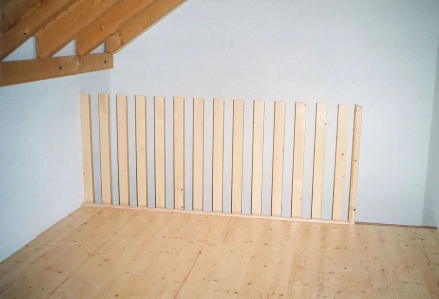 Grenier vide avec plafond en bois mansardé et une rangée de lattes de bois clair appuyées contre le mur