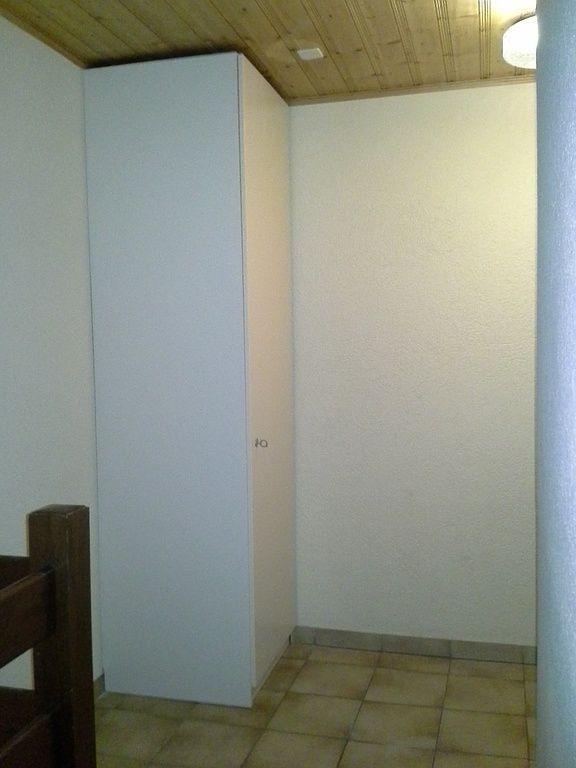 Petite pièce carrelée avec une haute armoire blanche contre un mur et un plafond en bois.