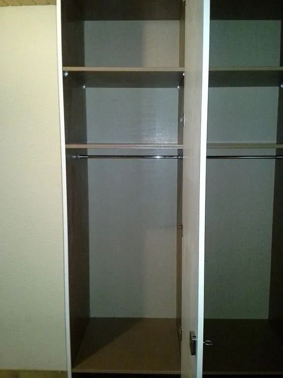 Armoire ouverte avec intérieur gris, étagères vides et tringles à vêtements.