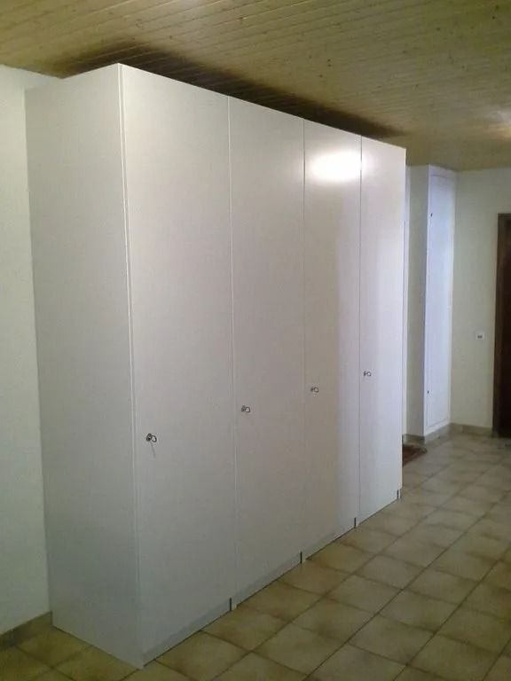 Des armoires de rangement blanches longent un couloir carrelé, à côté d'un mur et d'une porte.