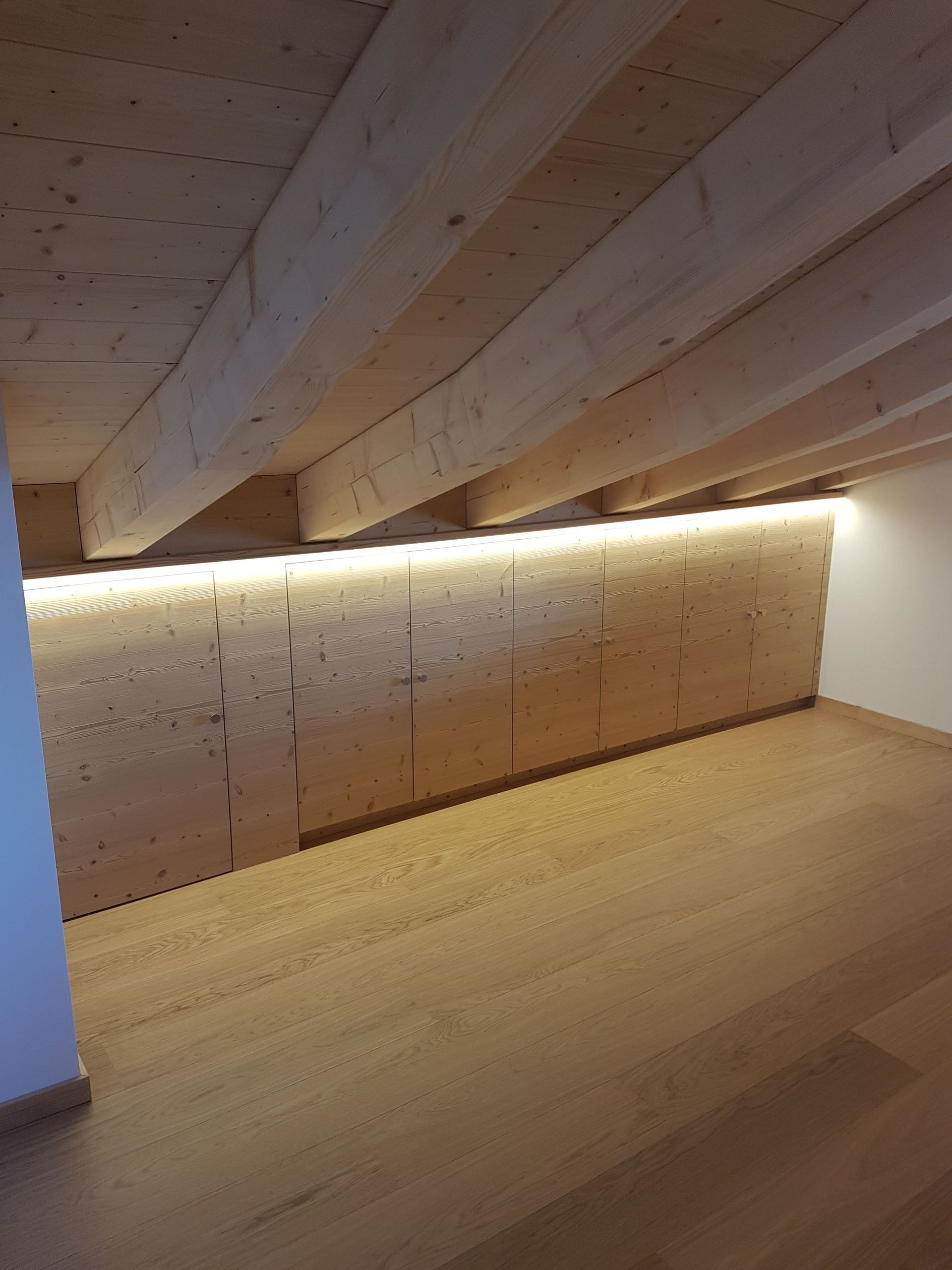 Alcôve en pente lambrissée avec un bandeau lumineux LED à lumière chaude le long du mur et du plafond.