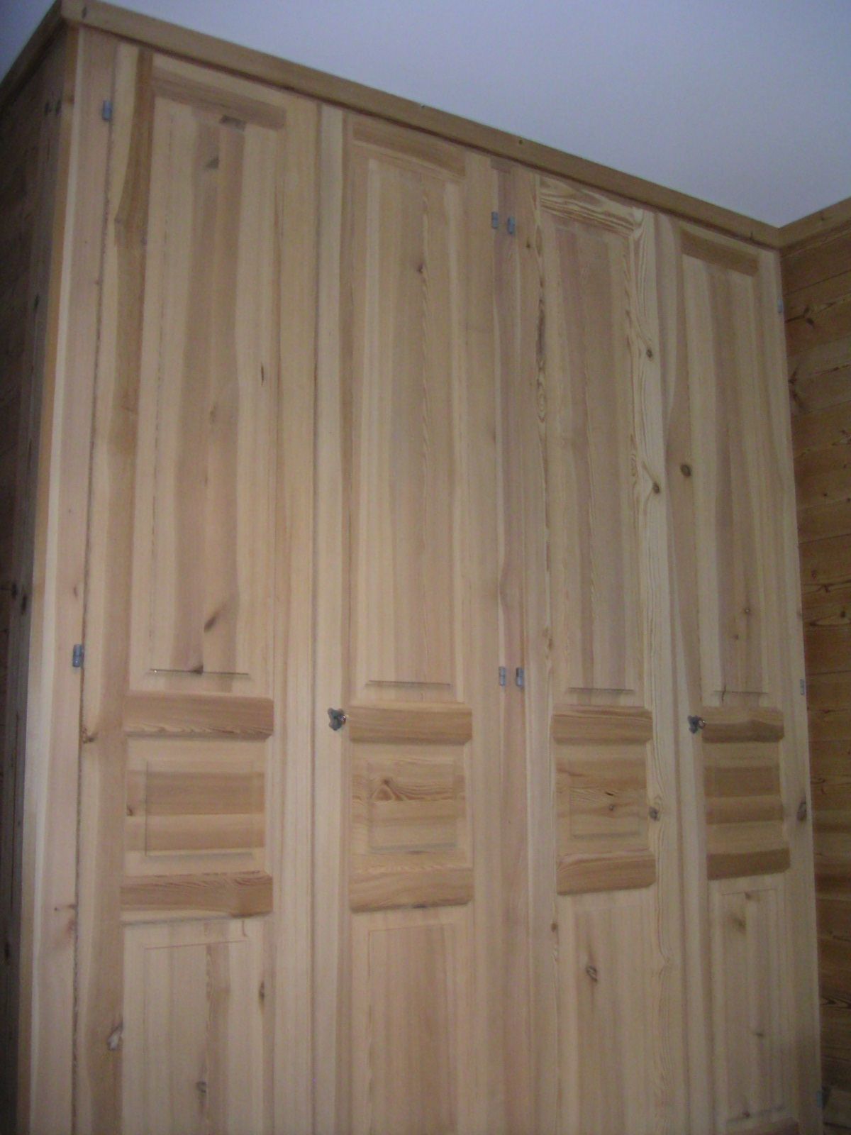 Portes de placard à panneaux de bois dans un coin de pièce, avec un grain de bois naturel clair et de petits panneaux horizontaux.