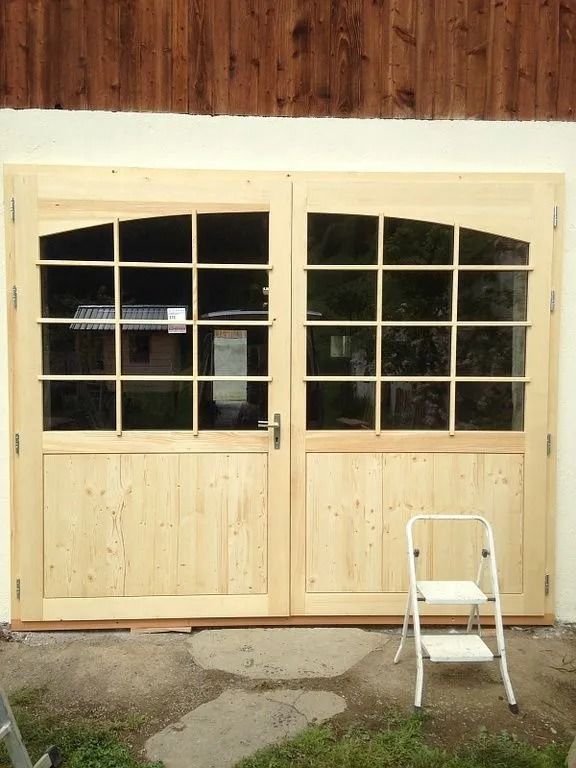Portes doubles vitrées en bois clair avec fenêtres, et un marchepied blanc sur le béton extérieur.