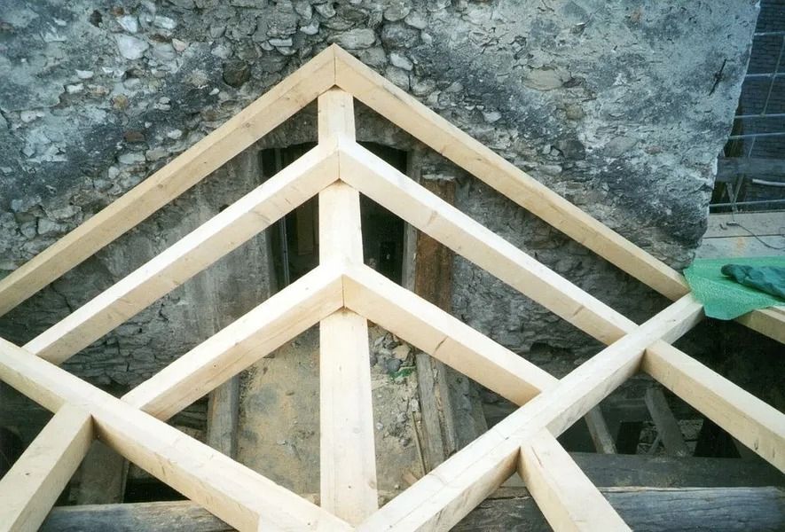 Charpente de toit en bois avec poutres diagonales appuyée contre un mur en pierre brute