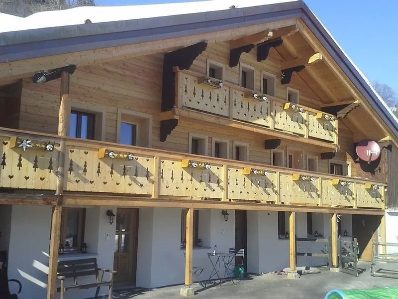 Chalet en bois avec deux balcons et balustrades jaunes dans un cadre montagneux ensoleillé