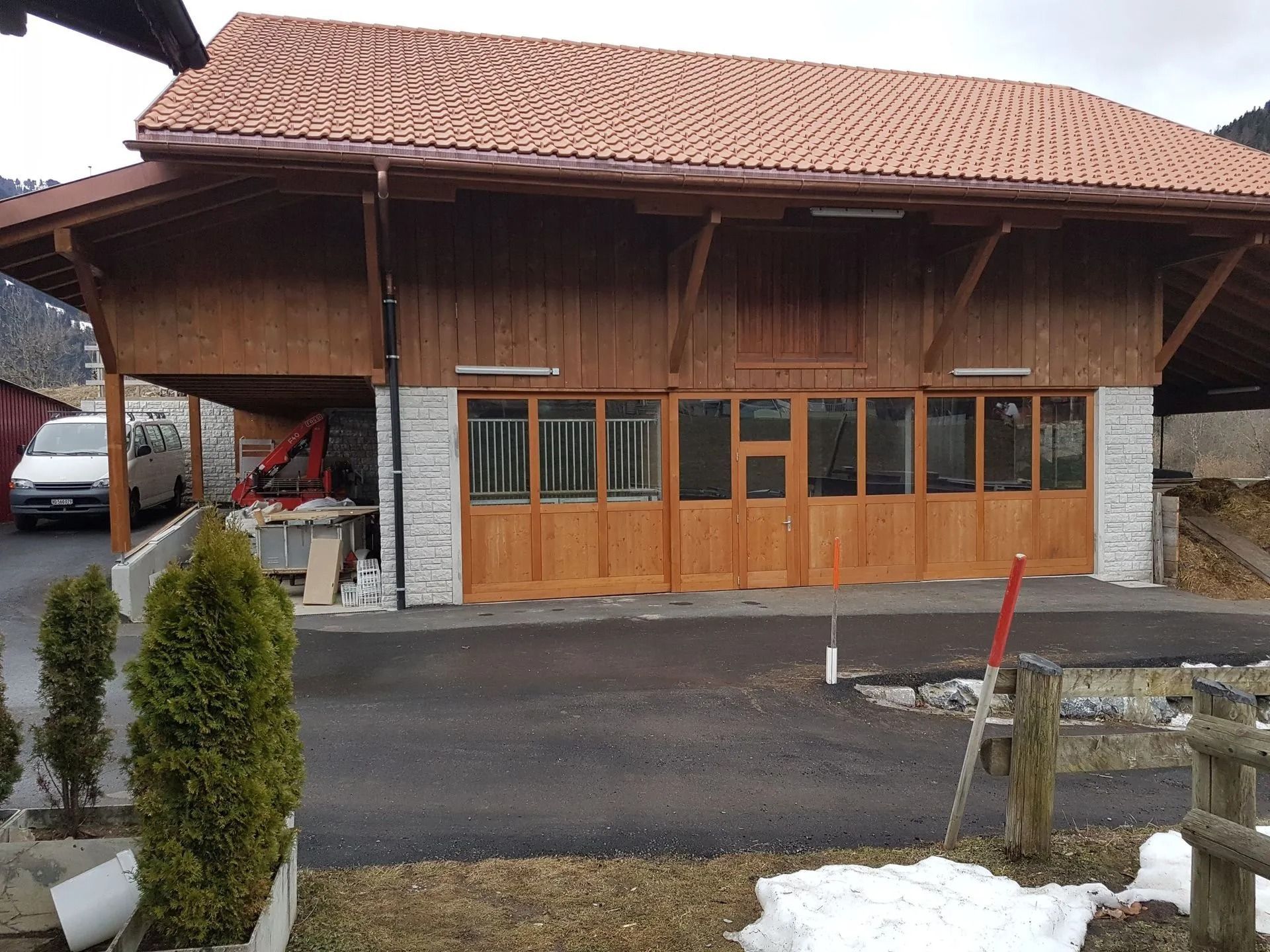 Maison en bois avec toit de tuiles, portes de style garage et allée carrossable à l'avant.
