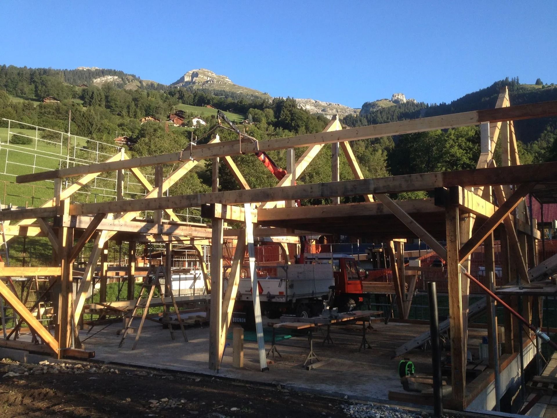 Charpente en bois en construction dans un cadre rural montagneux avec des collines verdoyantes et des falaises rocheuses en arrière-plan