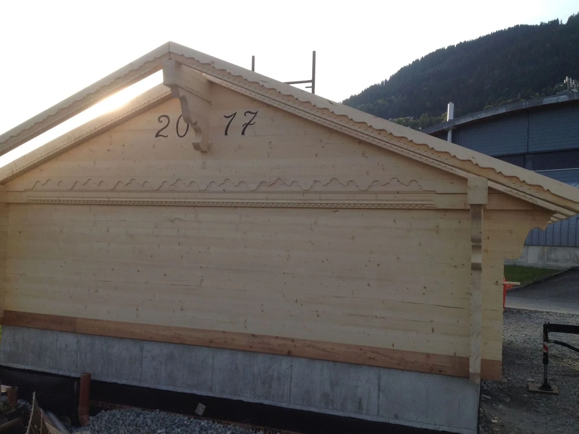 Abri en bois avec un toit à pignon et le numéro 2077 sur la façade, au bord d'une route de montagne.