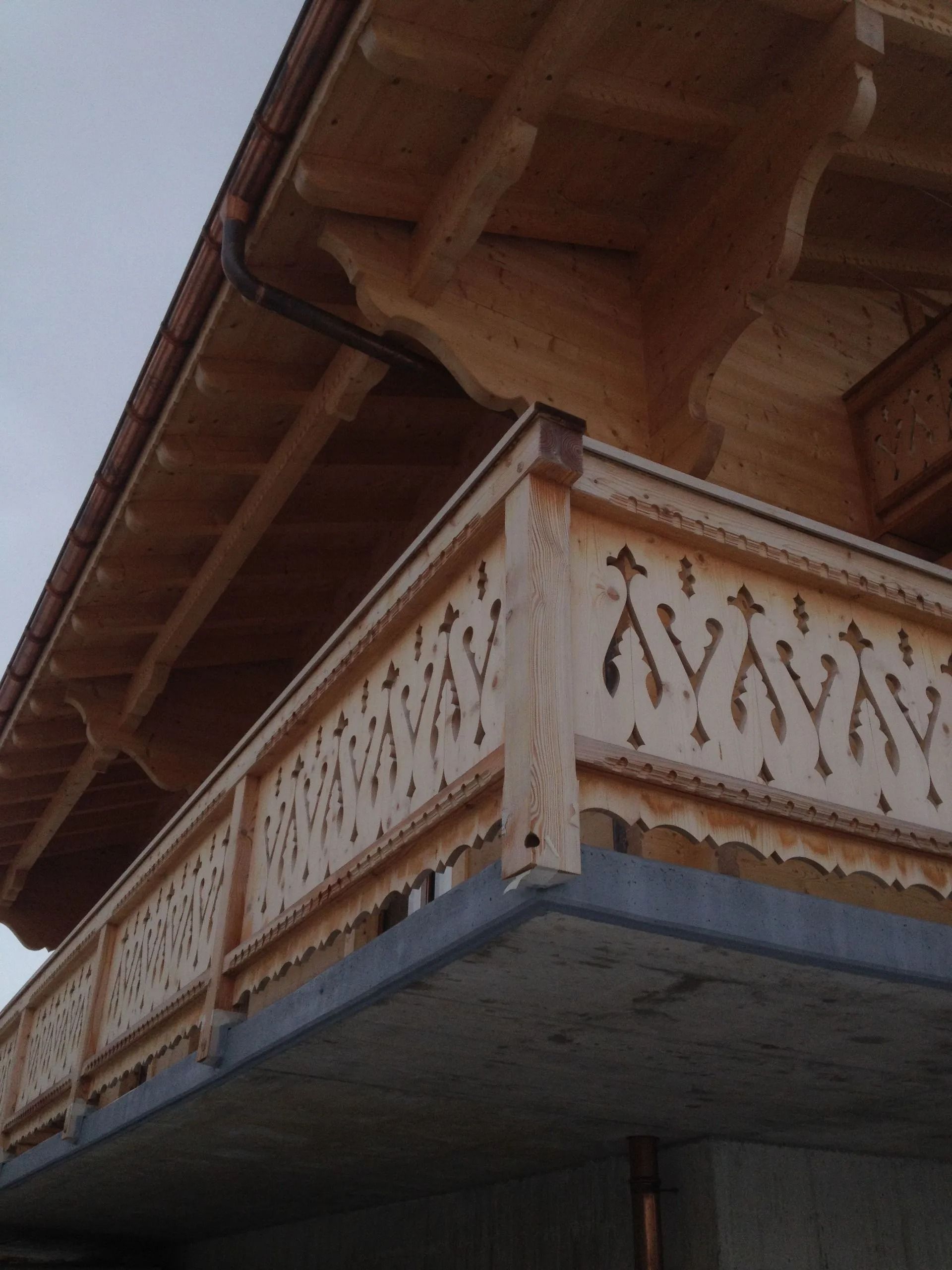 Balcon en bois orné avec balustrade blanche sculptée sous un toit en pente