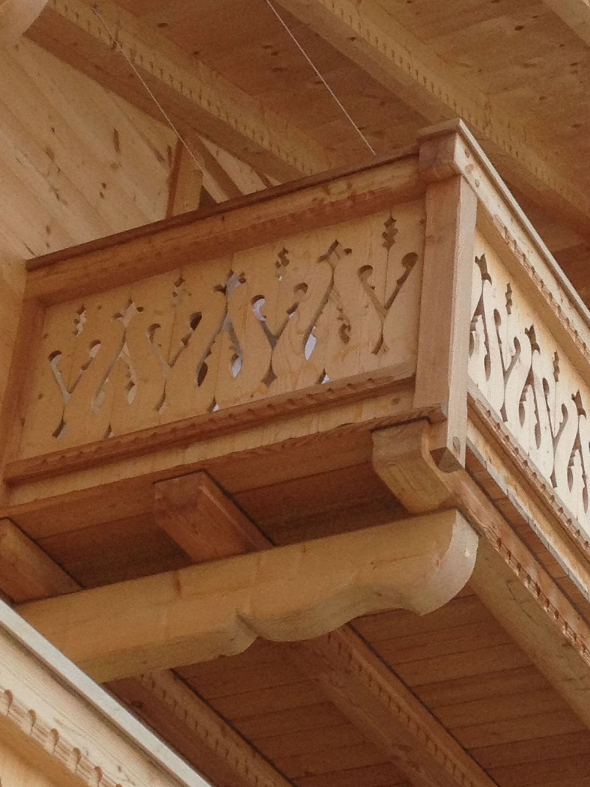 Rambarde de balcon en bois ornée de détails sculptés sur un plafond intérieur en bois