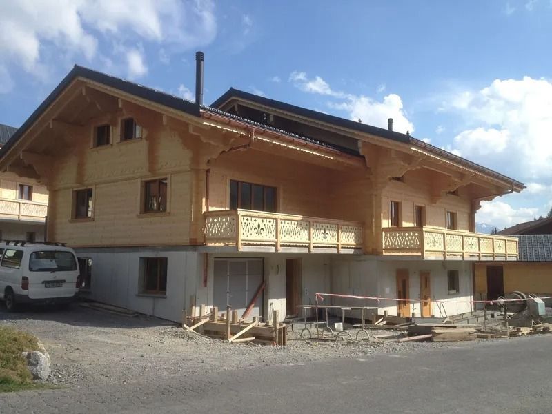 Maison de style chalet en bois avec balcons, fourgonnette garée et cour gravillonnée sous un ciel bleu