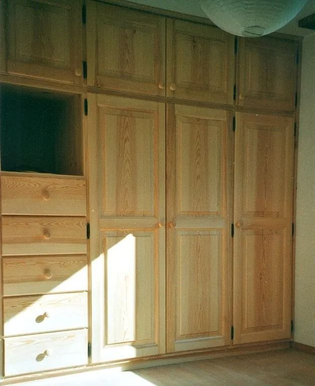 Armoires et commode encastrées en bois dans une chambre, la lumière du soleil projetant une ombre en diagonale.