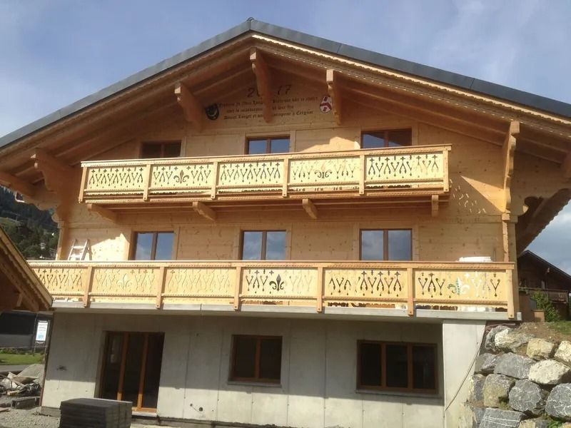 Maison de style chalet en bois avec balcons sculptés et fondations en pierre sous un ciel dégagé