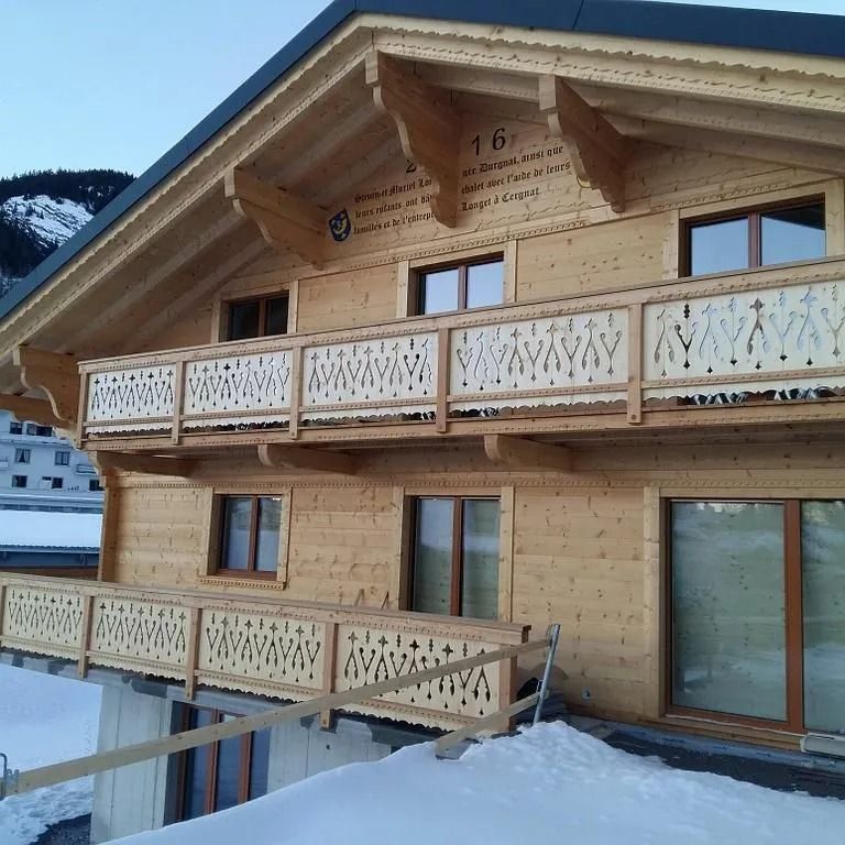 Chalet en bois enneigé avec balcons et balustrades décoratives dans un cadre montagnard