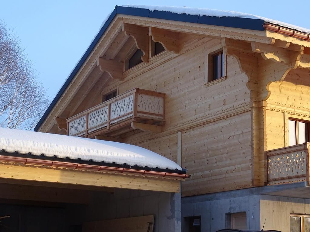 Maison en bois enneigée avec balcons et toit bleu sous un soleil éclatant