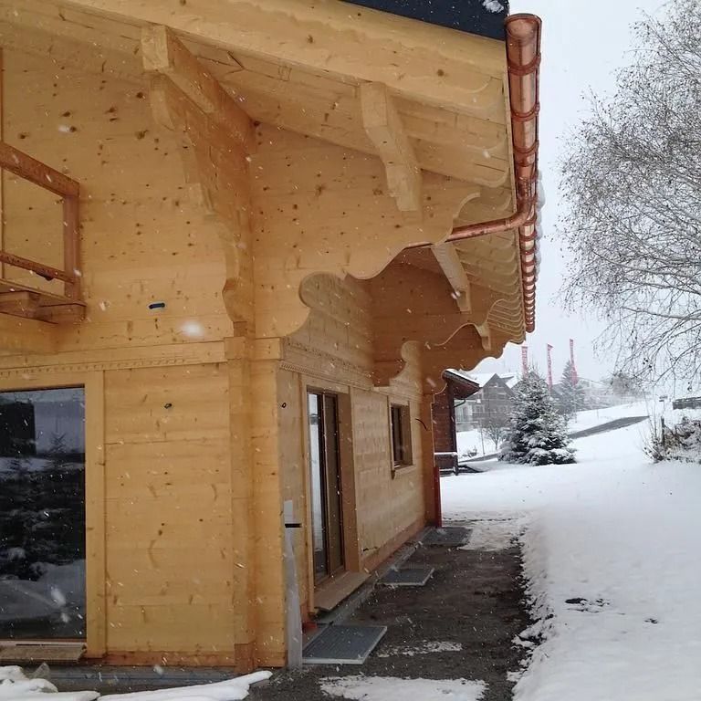 Extérieur d'une maison en bois avec avant-toit sculpté, cour enneigée et paysage hivernal