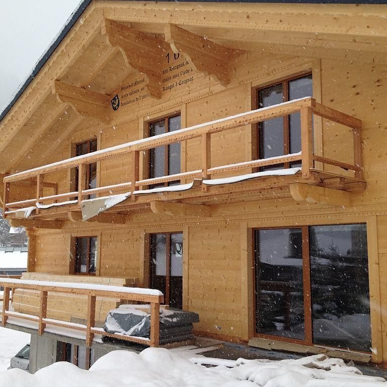 Chalet en bois enneigé avec balcons et grandes fenêtres sous un toit en pente
