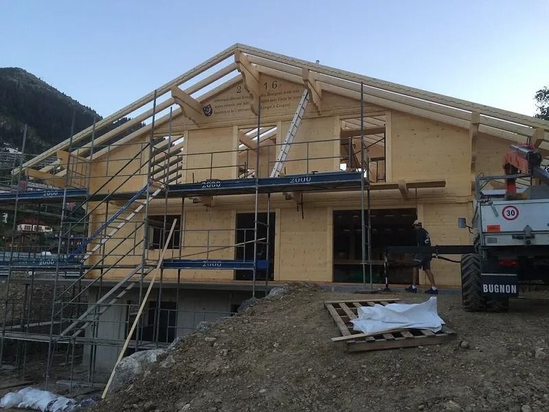 Maison en construction avec échafaudages et charpente de toit sur un terrain en terre battue