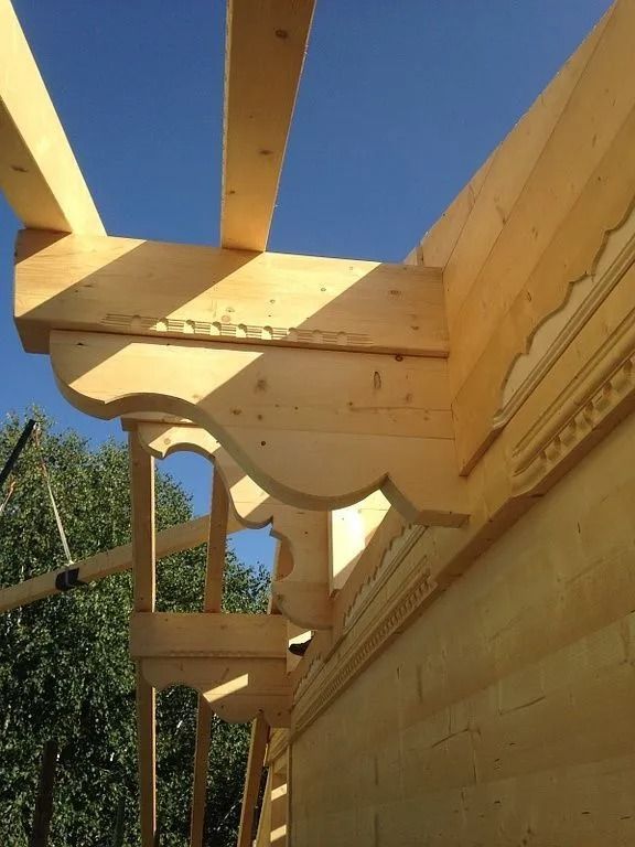 Poutres de toit en bois et ornements sculptés sur un bâtiment en construction, se détachant sur un ciel bleu.