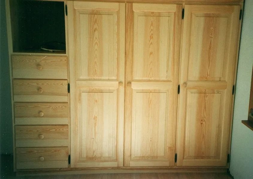 Armoire de chambre en bois à trois portes, à côté d'une commode et d'une petite étagère ouverte.