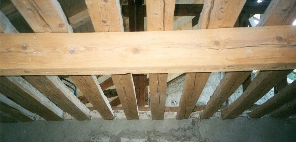 Chevrons et poutres de toit en bois à l'intérieur d'un grenier ou d'un vide sanitaire au-dessus d'un mur en béton.