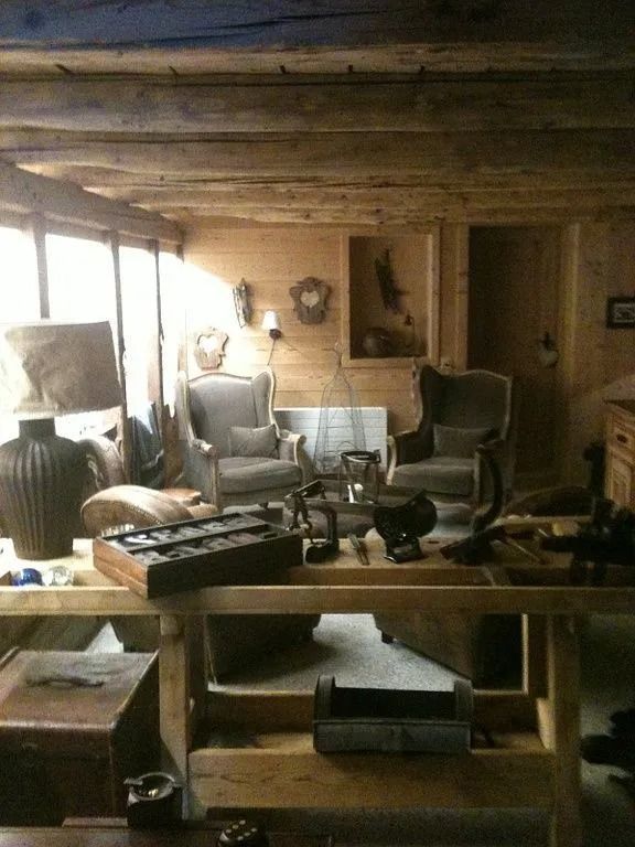 Salon rustique de chalet avec poutres en bois, fauteuils et petite table près d'une fenêtre.