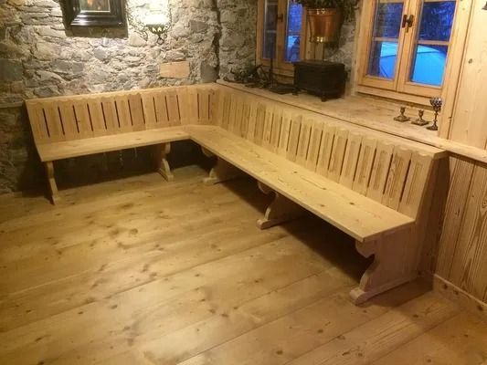 Banquette en bois en forme de L dans une pièce rustique en pierre avec fenêtre et parquet