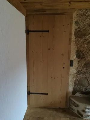 Porte en bois avec charnières noires dans un couloir rustique en pierre et plâtre