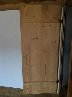 Porte d'armoire ou de placard en bois dans un intérieur rustique, entre un mur blanc et une porte sombre