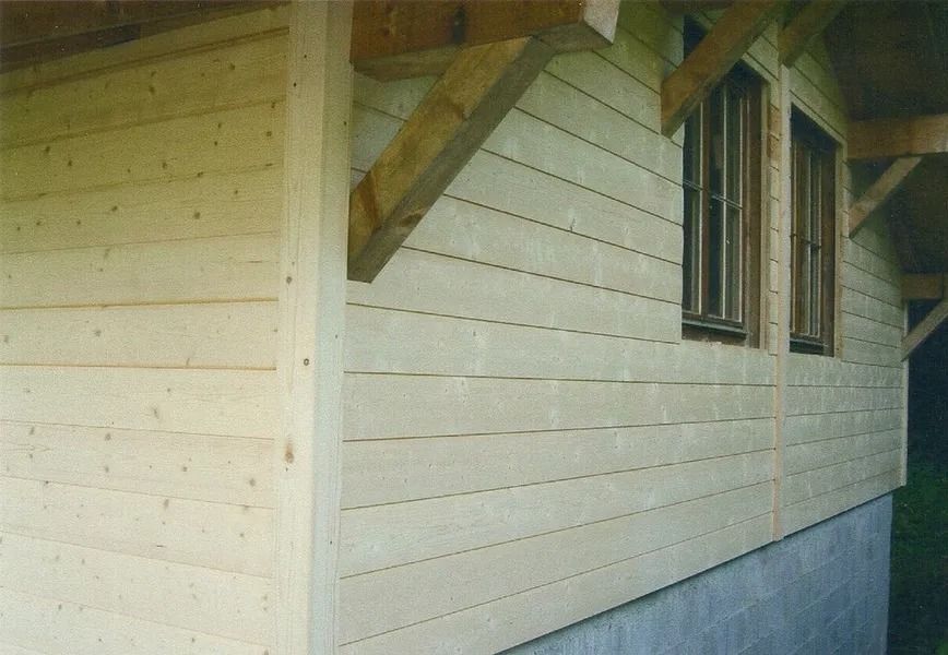 Maison de couleur crème avec bardage horizontal, petite fenêtre et avant-toit couvert sur fondations en béton.