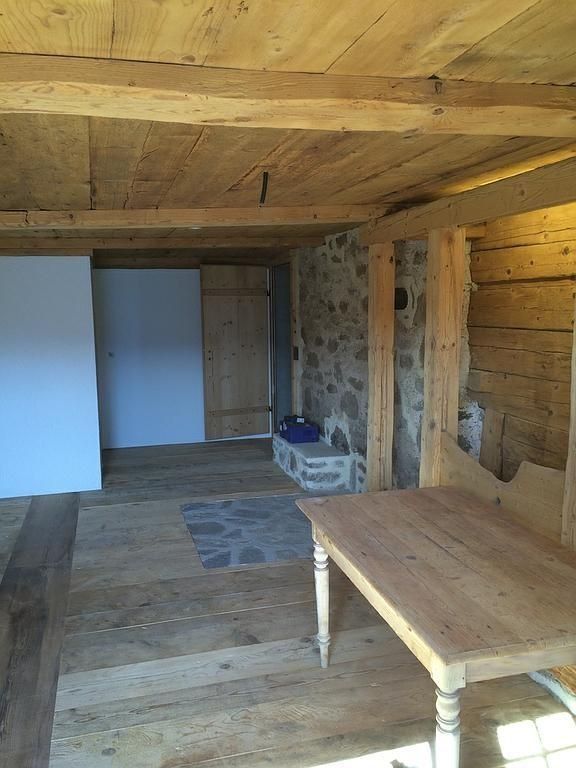 Intérieur rustique d'une pièce avec poutres en bois, mur en pierre, table et porte ouverte