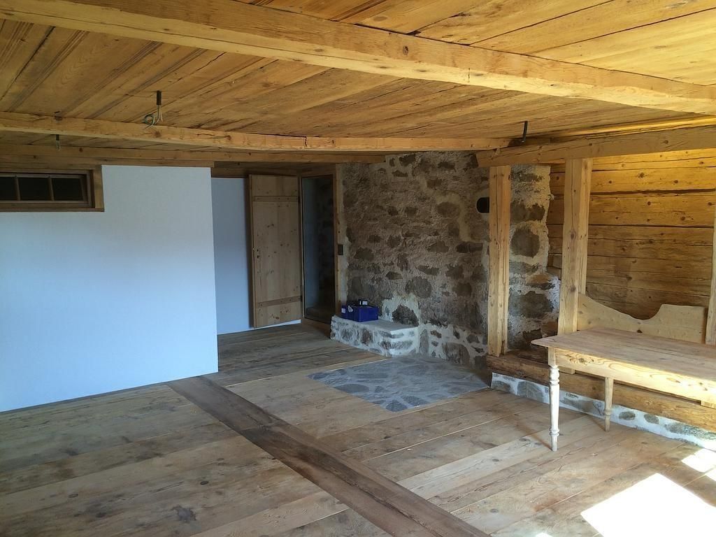 Pièce rustique avec mur en pierre, poutres en bois, cloison blanche et table en bois sous un plafond bas.