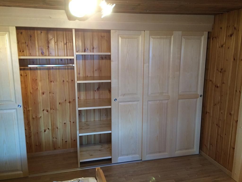 Placard en bois vide avec étagères ouvertes, tringle à vêtements et portes à panneaux blancs dans une pièce lambrissée