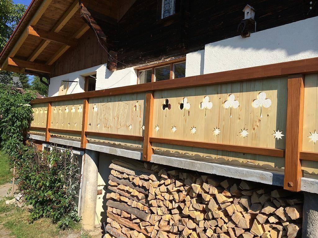 Rambarde de balcon en bois à panneaux sculptés au-dessus d'un mur de bûches empilées à côté d'une maison