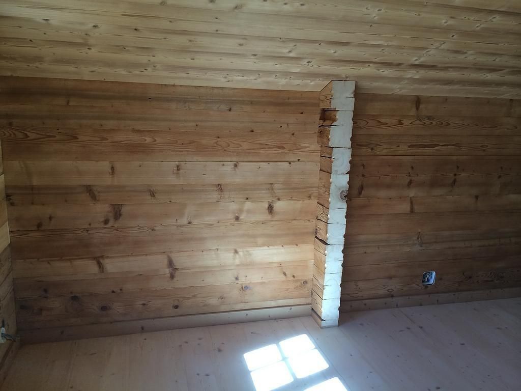 Pièce en bois vide, aux murs en planches, avec une colonne en briques blanches et la lumière du soleil sur le sol.