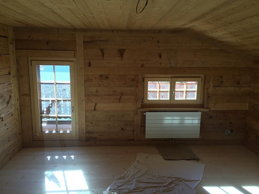 Pièce en bois vide avec une porte, une fenêtre et un radiateur blanc, la lumière du soleil inondant le sol.