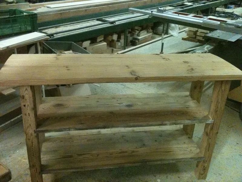 Étagère en bois dans un atelier, avec des planches brutes et des outils en arrière-plan.