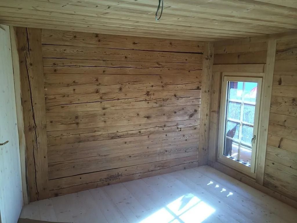 Pièce en bois vide, aux murs, au plafond et au sol en planches, éclairée par la lumière du soleil à travers une fenêtre.