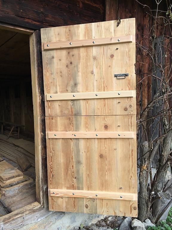 Porte en bois avec charnières métalliques encastrée dans une entrée rustique en pierre et en bois
