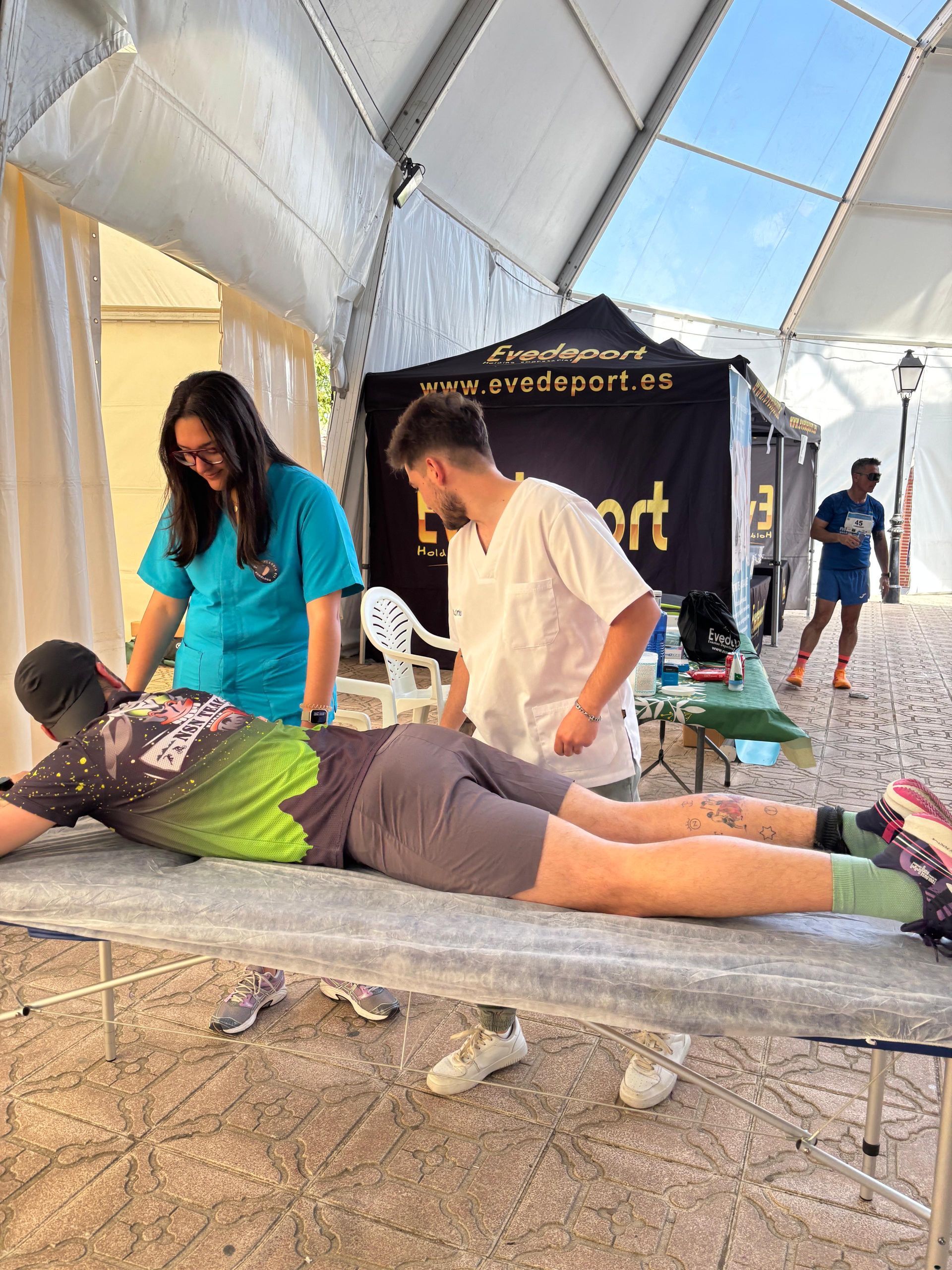 Dos personas dando un masaje sobre una esterilla dentro de una carpa en un evento al aire libre.
