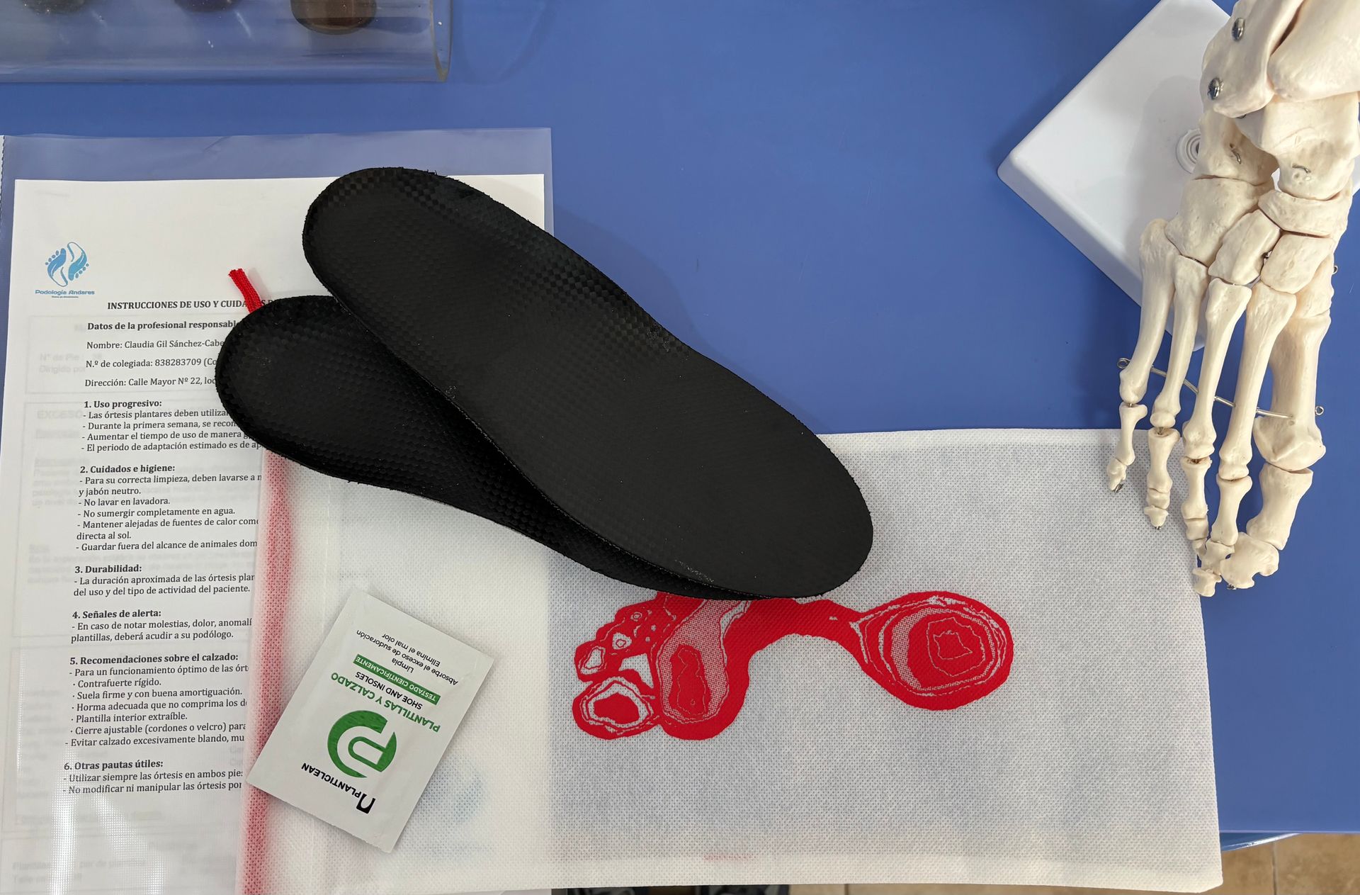 Plantillas negras, documentación, una tarjeta verde y una venda roja sobre una superficie azul con un modelo de pie esquelético.
