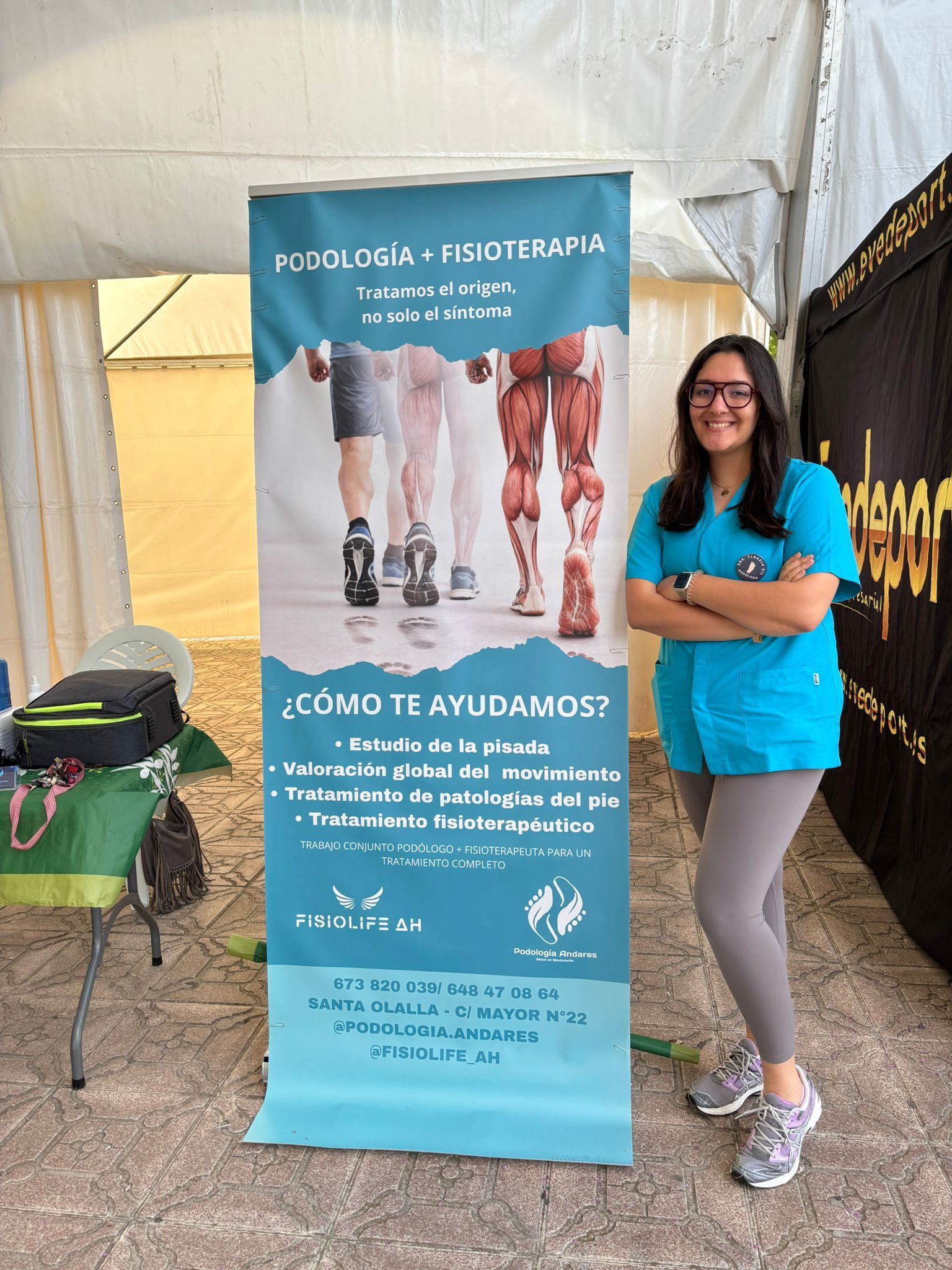 Una mujer con uniforme médico azul está de pie junto a una pancarta médica de color turquesa en un área de eventos techada.