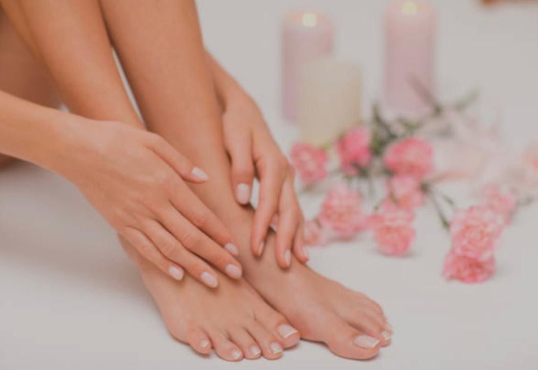 Hände streicheln Füße; weiche Haut. Rosa Nelken und Kerzen im Hintergrund.