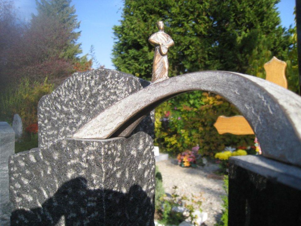 Une statue d'une femme debout au sommet d'un pont dans un cimetière.