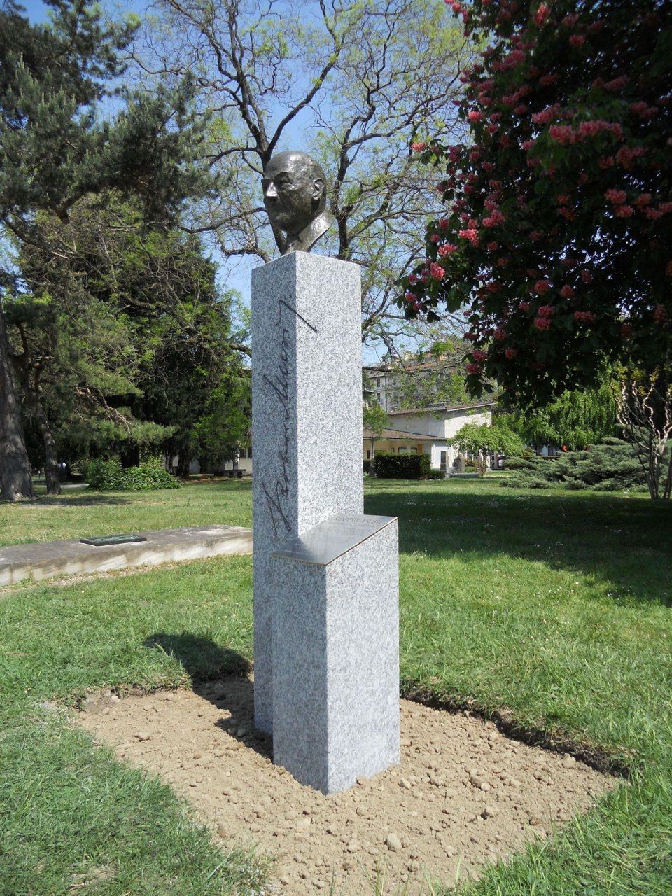 Une statue représentant une tête d'homme se trouve au sommet d'un pilier de pierre dans un parc.