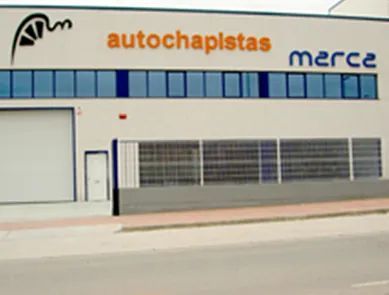 Un edificio industrial blanco con una hilera de ventanas tintadas de azul y un letrero que dice 