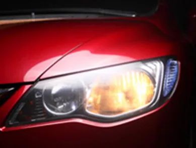 Primer plano de un faro amarillo brillante sobre el capó rojo brillante de un coche.