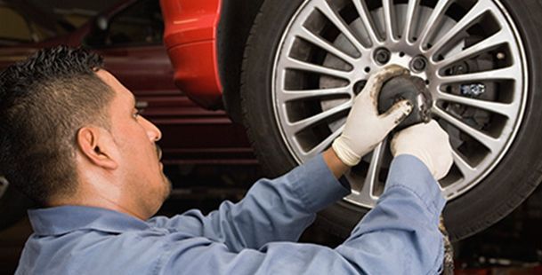 Un mecánico con camisa azul y guantes blancos utiliza una llave de impacto para apretar una tuerca de la rueda de un coche.