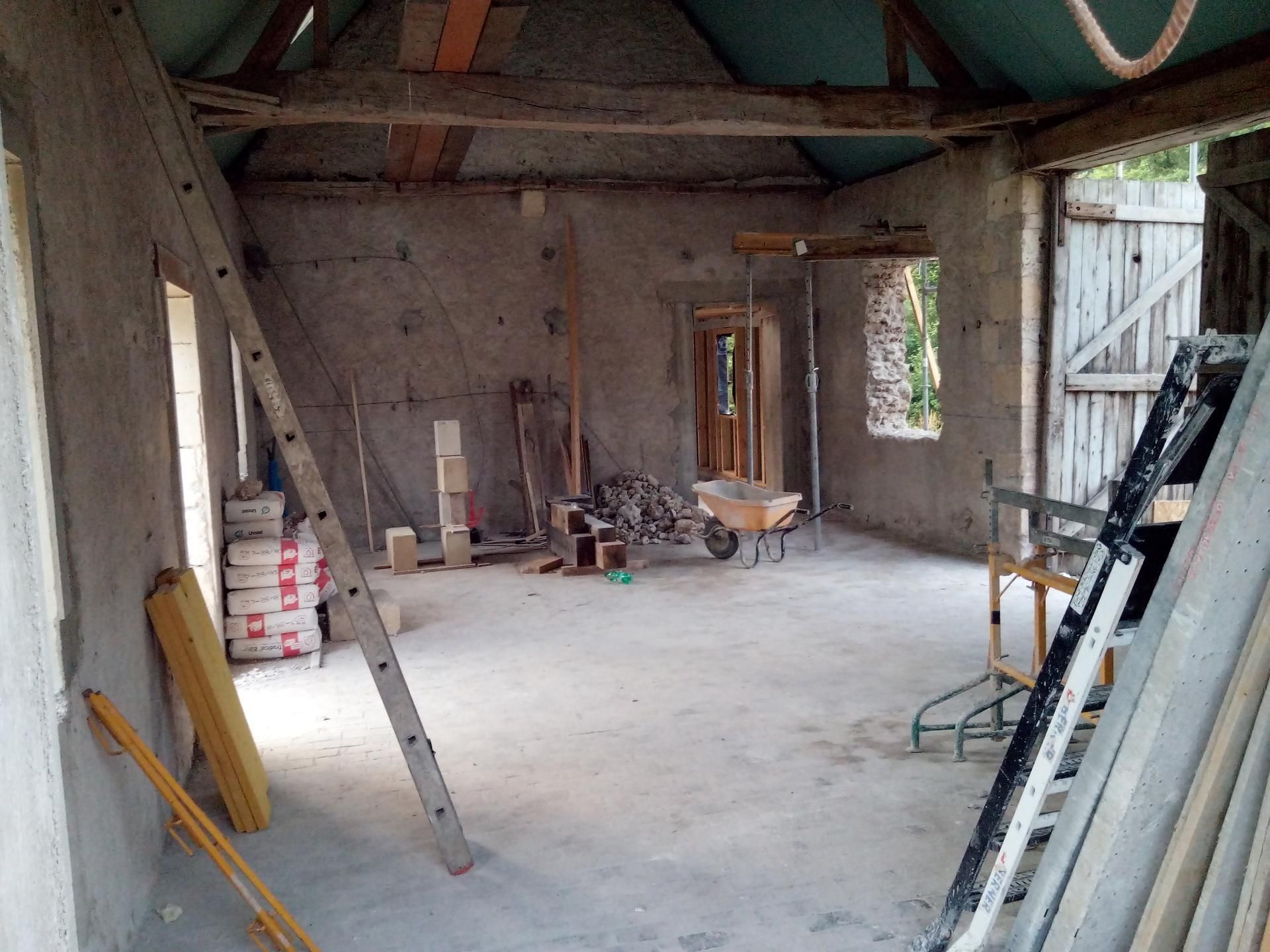 Intérieur d'une pièce en construction, avec des murs en béton, des poutres en bois et des matériaux de construction.