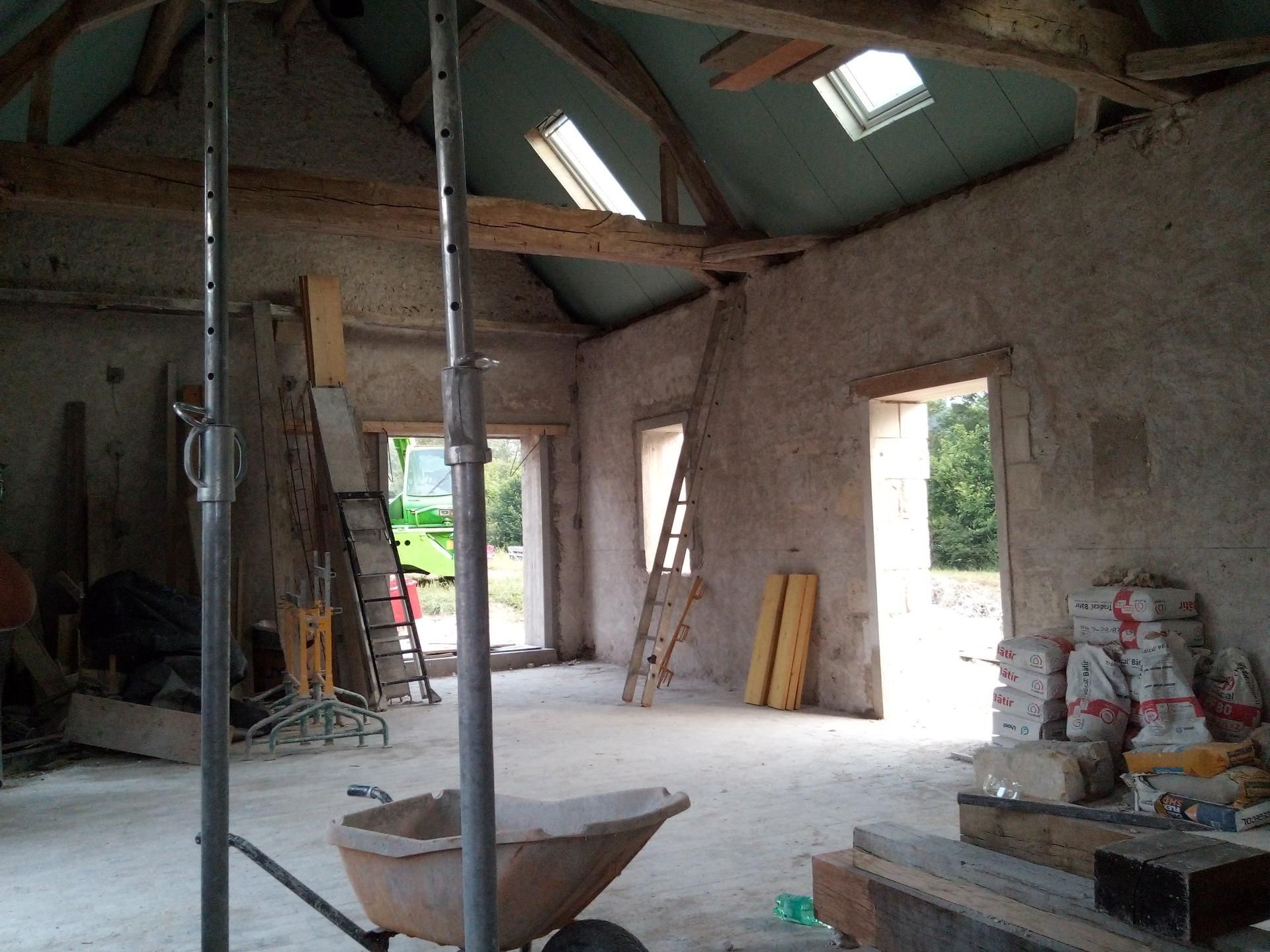 Intérieur d'un bâtiment en rénovation avec poutres apparentes, portes ouvertes et matériaux de construction.